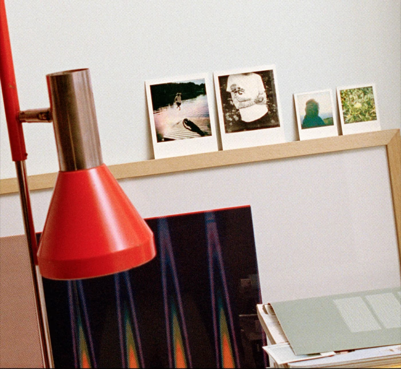 Original film-grain photograph of a red lamp and instant prints on a wooden shelf